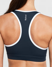 Navy sports bra with white straps on a model against a light gray background