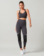Woman wearing a black sports bra and leggings on a gray background