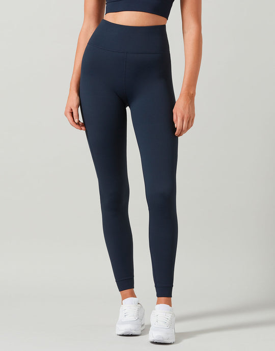 Person wearing navy leggings and a dark top on a light gray background
