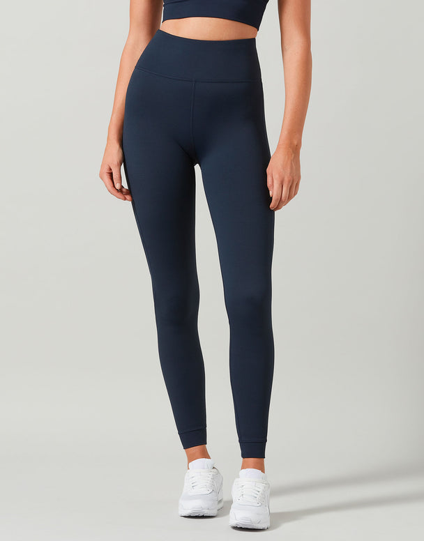 Person wearing navy leggings and a dark top on a light gray background