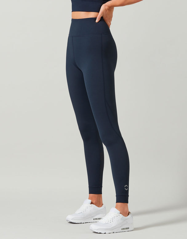 Person wearing navy leggings and white sneakers on a gray background