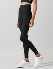 Person wearing black leggings with white sneakers on a gray background