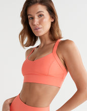 Woman wearing a coral sports bra and leggings on a light gray background