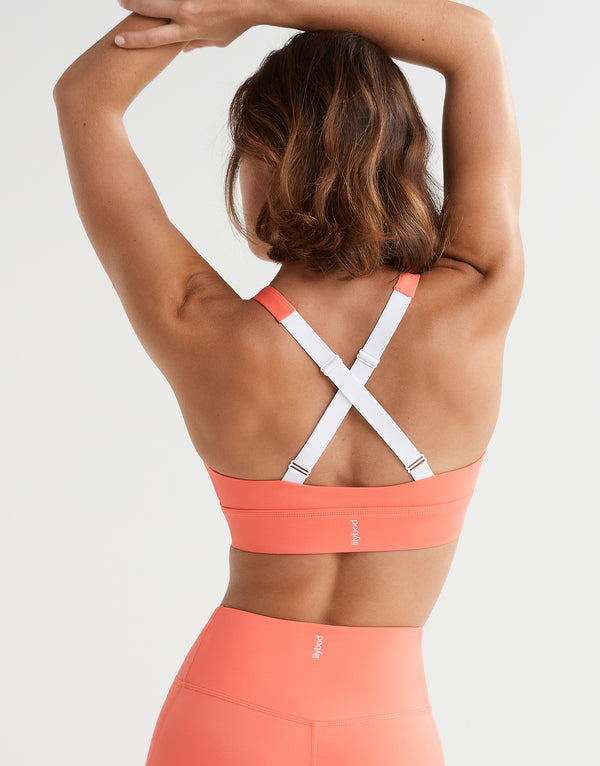 Woman wearing a coral sports bra and leggings with a white background