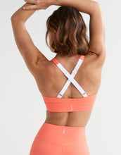 Woman wearing a coral sports bra and leggings with a white background