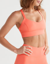 Woman wearing a coral sports bra and leggings on a light gray background