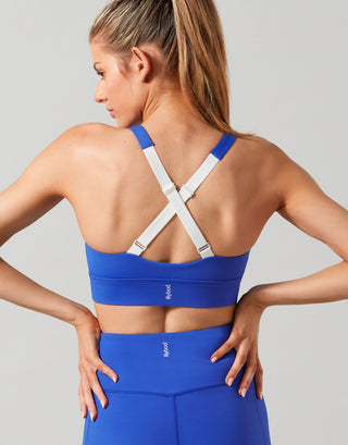 A model wearing a cobalt blue sports bra with adjustable straps and a low cut V neckline, paired with matching blue activewear pants.