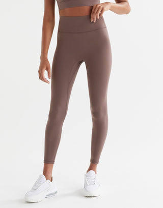 A person standing wearing brown tinted, high-waisted leggings and a matching sports bra. The leggings have a minimal seaming design and are made from a fabric blend of polyamide and lycra.