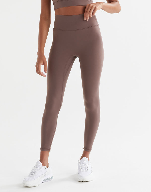 A person standing wearing brown tinted, high-waisted leggings and a matching sports bra. The leggings have a minimal seaming design and are made from a fabric blend of polyamide and lycra.
