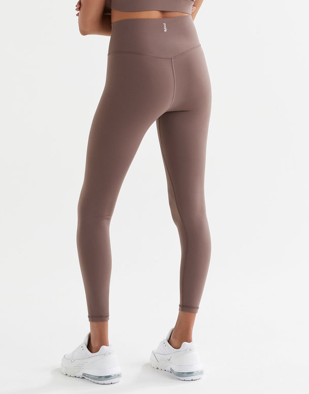A person standing wearing brown tinted, high-waisted leggings and a matching sports bra. 