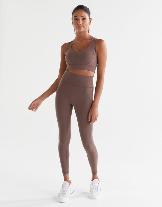 A model standing wearing brown tinted, high-waisted leggings and a matching sports bra. The leggings have a minimal seaming design and are made from a fabric blend of polyamide and lycra.