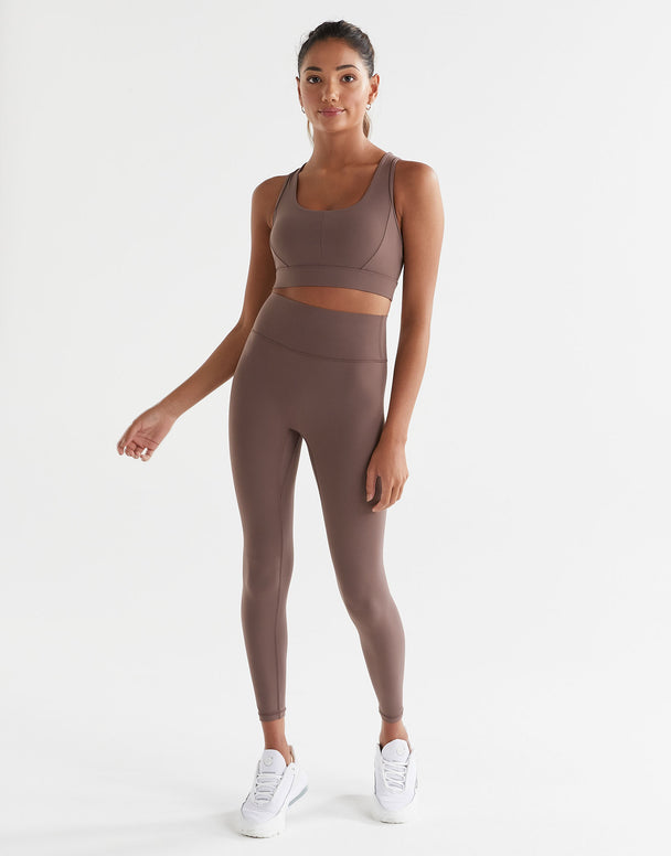 A model standing wearing brown tinted, high-waisted leggings and a matching sports bra. The leggings have a minimal seaming design and are made from a fabric blend of polyamide and lycra.