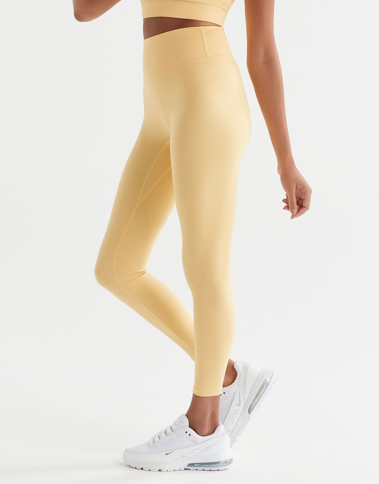 A pair of high-waisted yellow leggings with a minimal seaming design, designed for activewear with white sneakers.