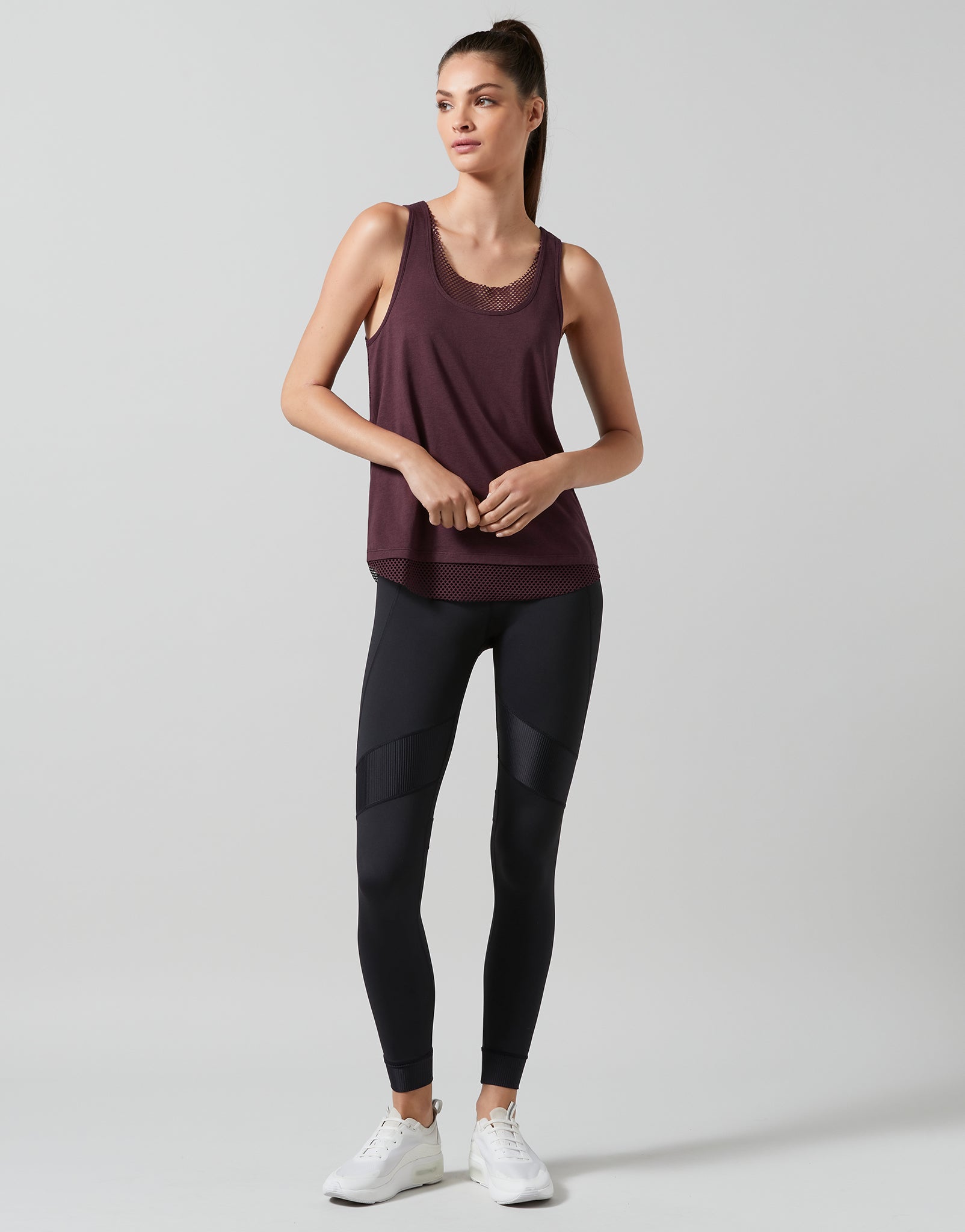 Woman wearing a maroon tank top and black leggings on a light gray background