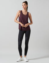 Woman wearing a maroon tank top and black leggings on a light gray background