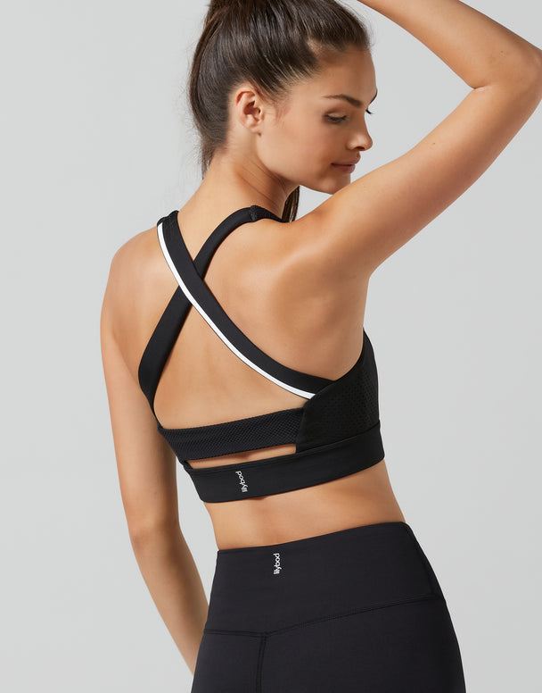 A woman shown from the back wearing a black sports bra with white trim and matching black athletic leggings, photographed against a light gray studio background.