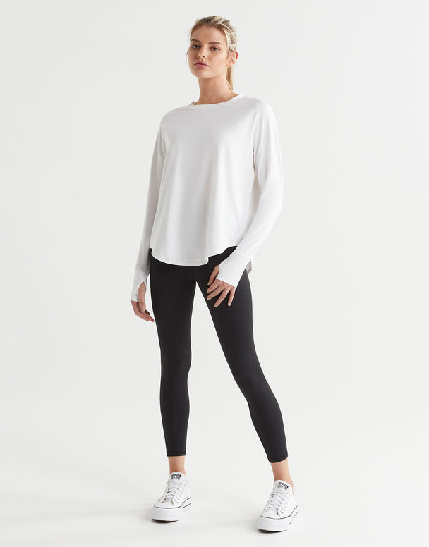 A female model wearing a long-sleeved white t-shirt with a round neckline, paired with black leggings and runners.