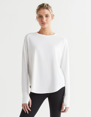 A female model wearing a long-sleeved white t-shirt with a round neckline, paired with black pants.