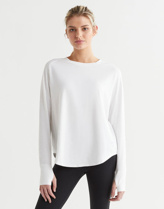 A female model wearing a long-sleeved white t-shirt with a round neckline, paired with black pants.