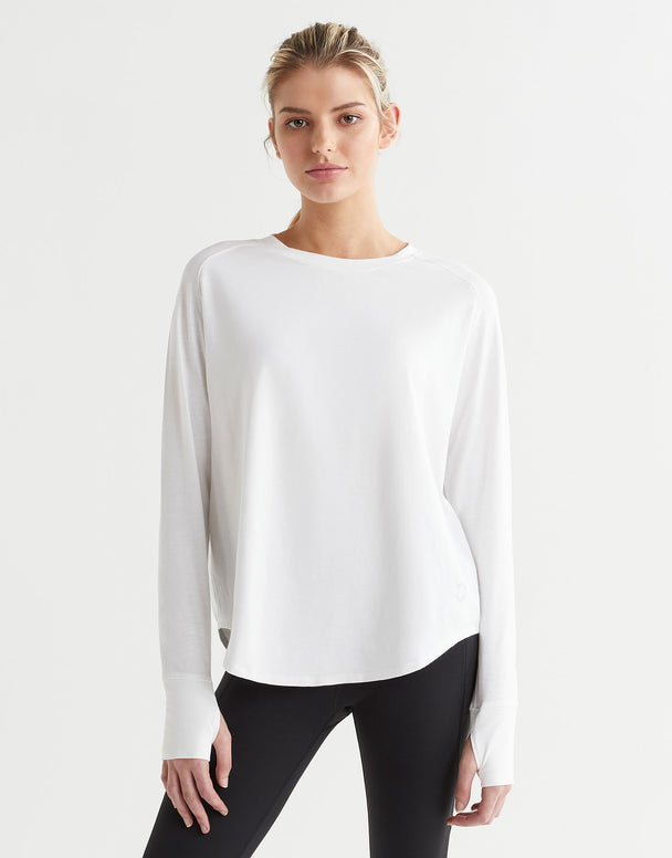 A female model wearing a long-sleeved white t-shirt with a round neckline, paired with black pants.