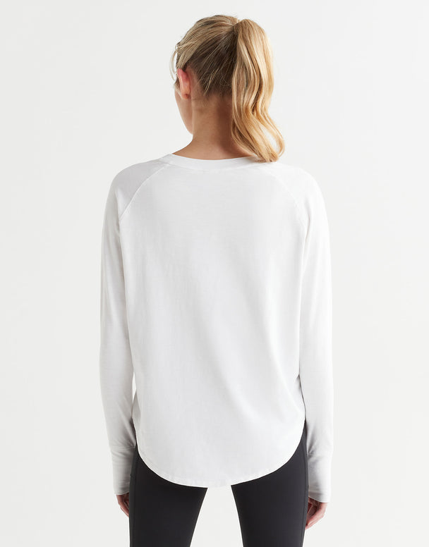 A female model wearing a long-sleeved white t-shirt with a round neckline, paired with black leggings.