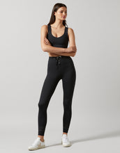 A woman wearing black tie-up activewear leggiings, a sports bra and white runners.