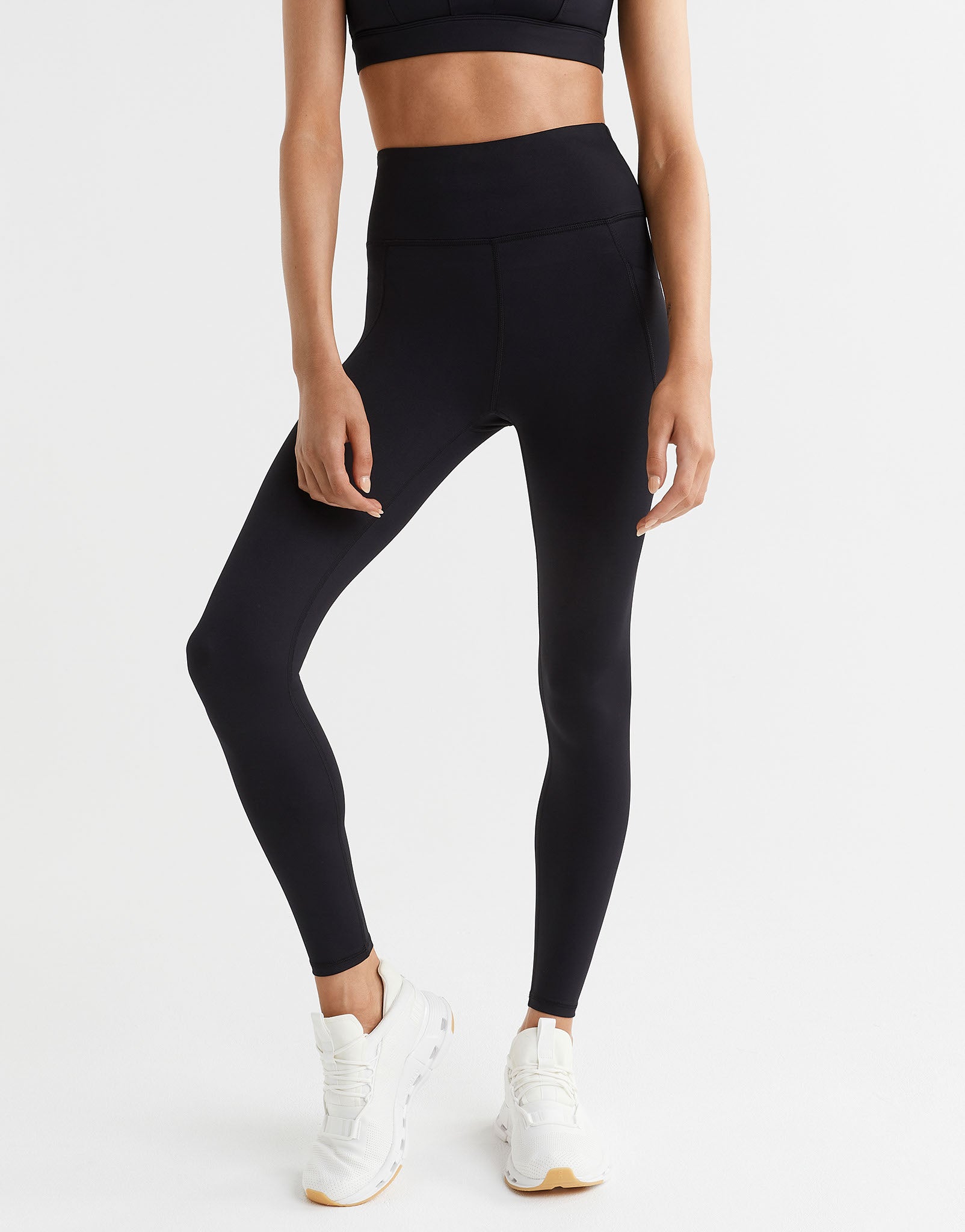 Person wearing black leggings and white sneakers on a white background