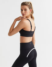 Woman wearing a black sports bra and leggings on a light gray background