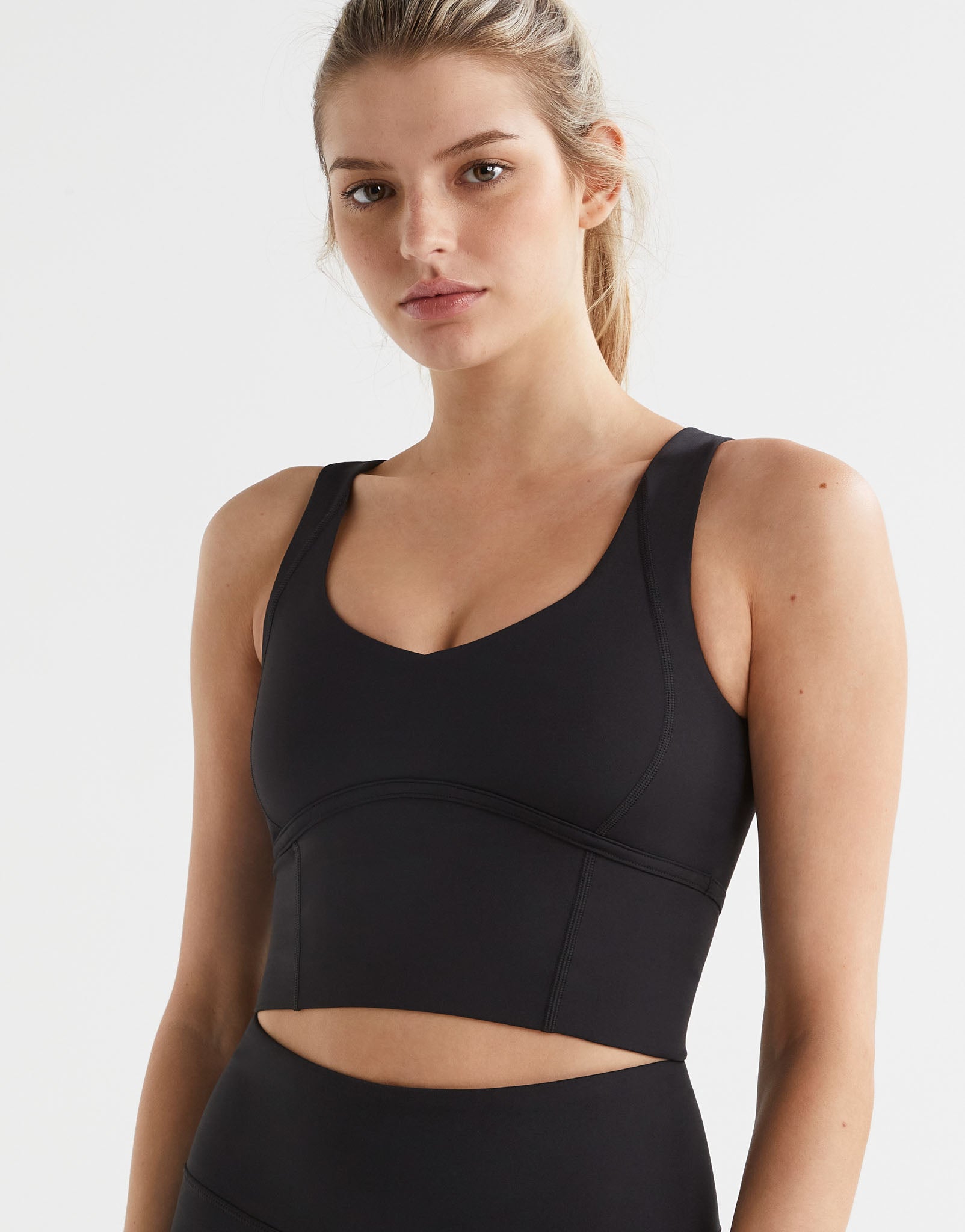 A woman wearing a black Lilybod Daisy Sports Bra with wide shoulder straps and a scoop neckline.