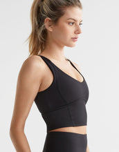Woman wearing a black sports bra and leggings on a light gray background