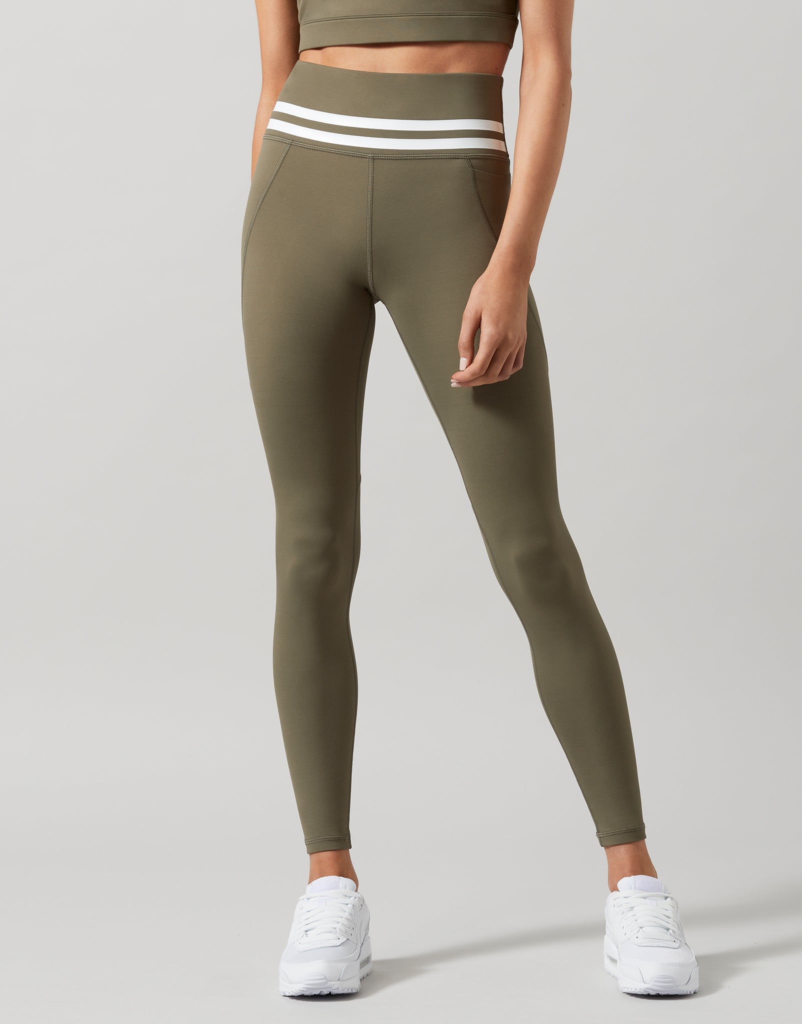 A pair of khaki green Lilybod Dakota leggings with a sports bra and white sneakers.