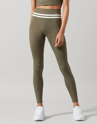 A pair of khaki green Lilybod Dakota leggings with a sports bra and white sneakers.