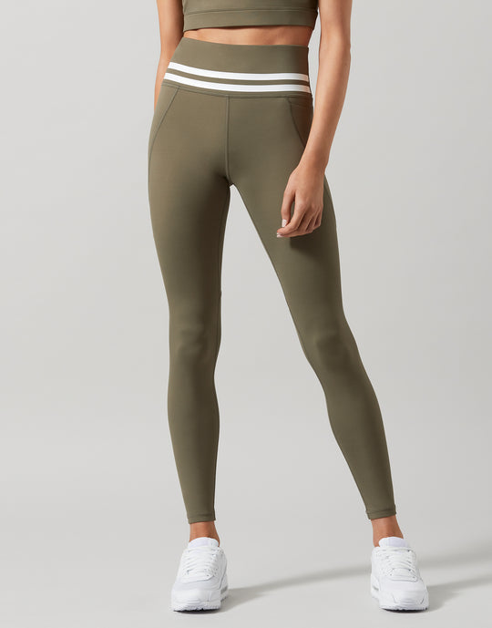 A pair of khaki green Lilybod Dakota leggings with a sports bra and white sneakers.
