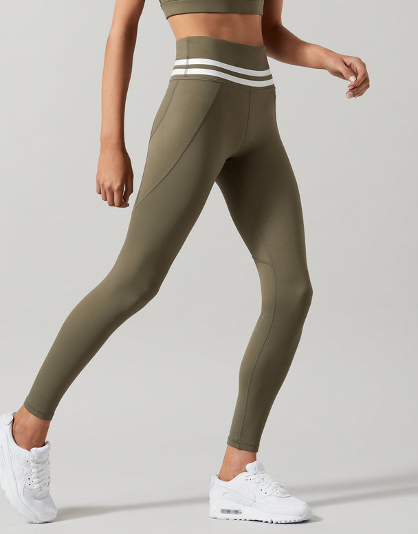 A pair of khaki green Lilybod Dakota leggings with a sports bra and white sneakers. Side view.