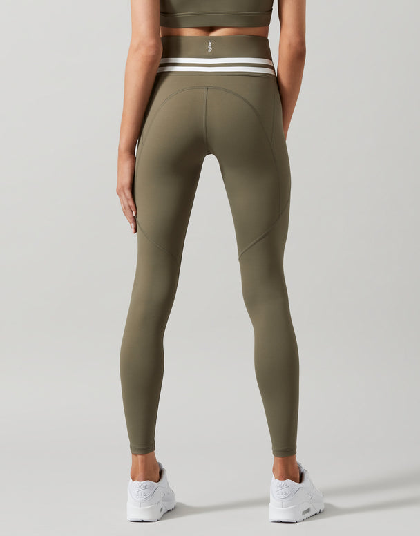 A pair of khaki green Lilybod Dakota leggings with a sports bra and white sneakers. Back view.