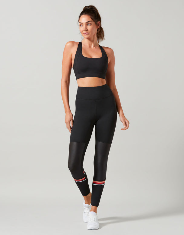 Woman wearing a black athletic outfit with leggings and sports bra on a light gray background