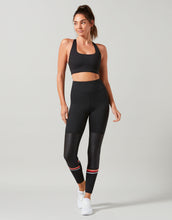 Woman wearing a black athletic outfit with leggings and sports bra on a light gray background