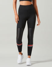 Person wearing black leggings with red accents on a gray background