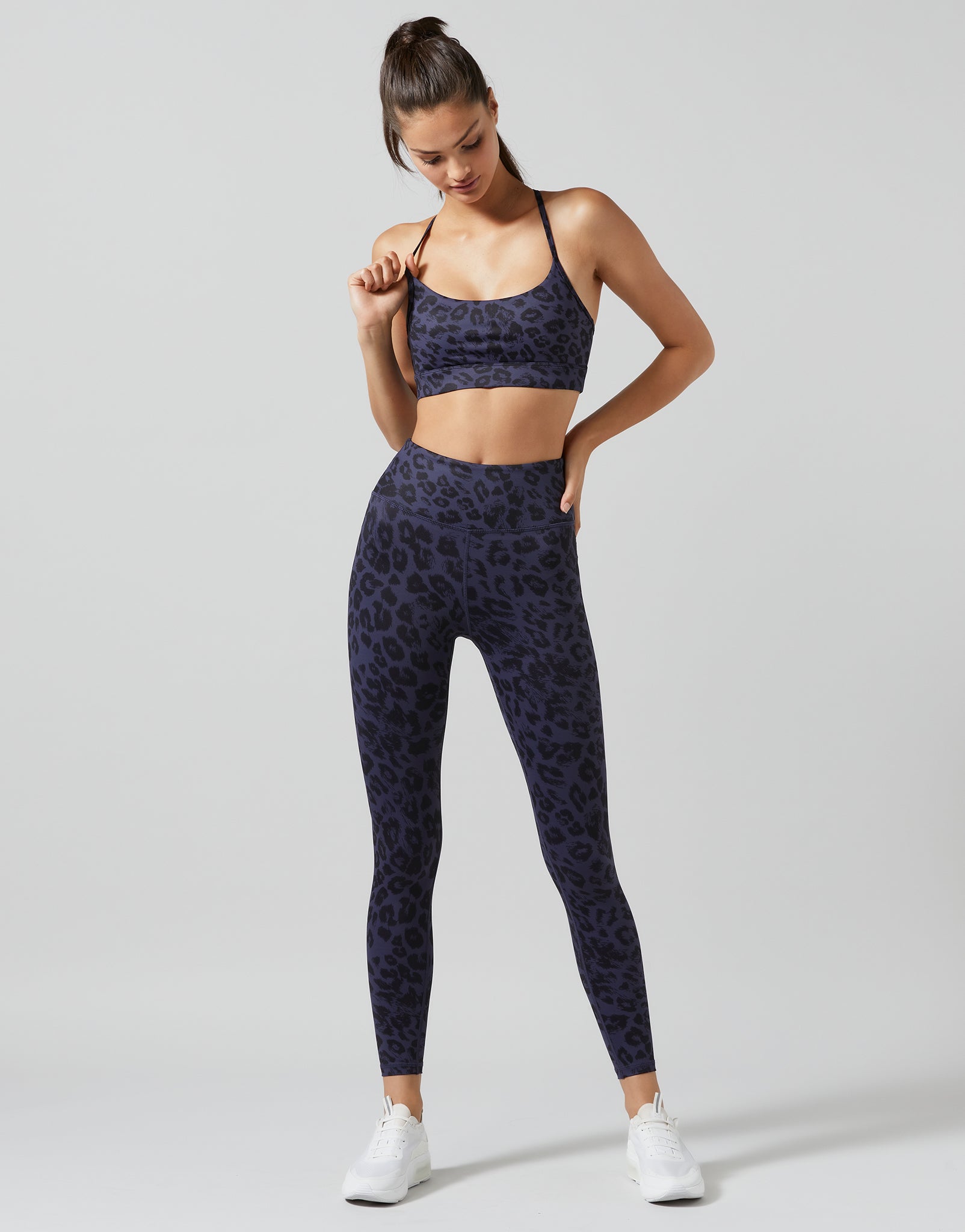 Woman wearing a navy blue sports bra and leggings with a pattern on a light gray background