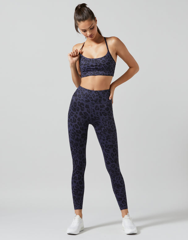 Woman wearing a navy blue sports bra and leggings with a pattern on a light gray background