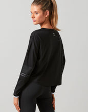 Woman wearing a black long-sleeve top and black leggings on a gray background