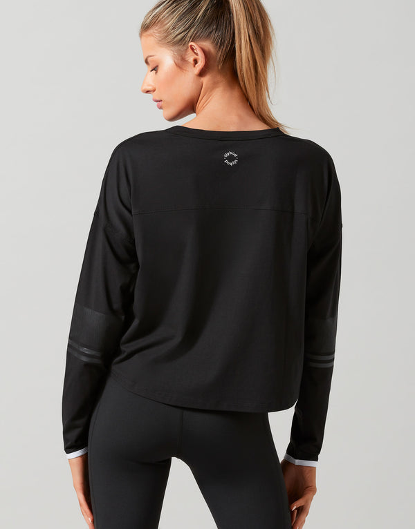 Person wearing a black long-sleeve top with a logo on the back against a gray background