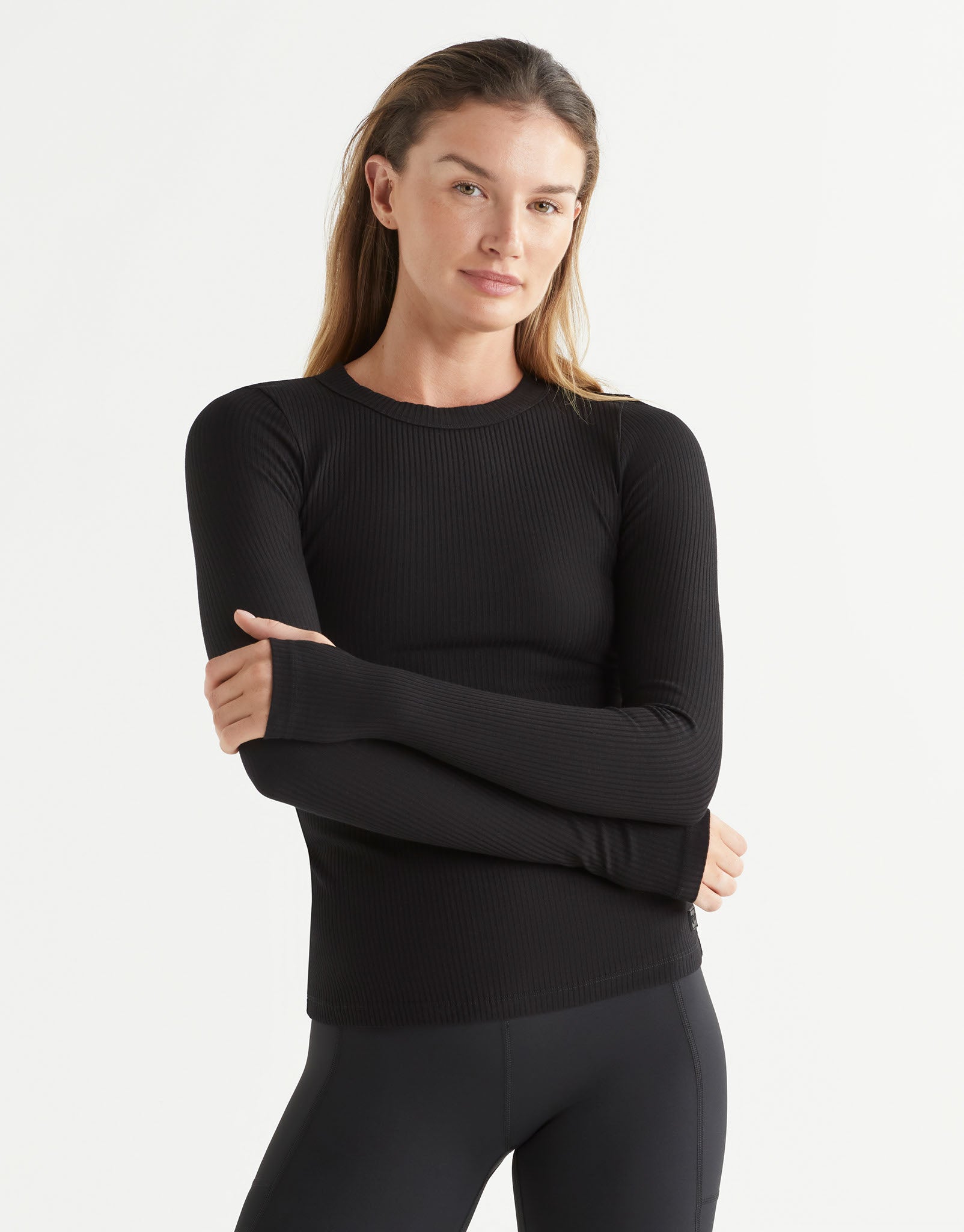 Woman wearing a black long-sleeve top and black leggings on a white background