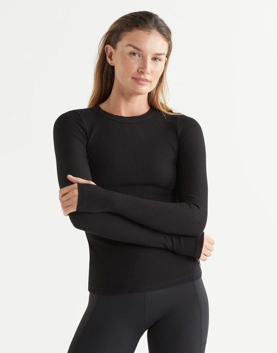 Woman wearing a black long-sleeve top and black leggings on a white background