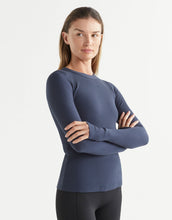 Woman wearing a blue long-sleeve top with arms crossed on a white background