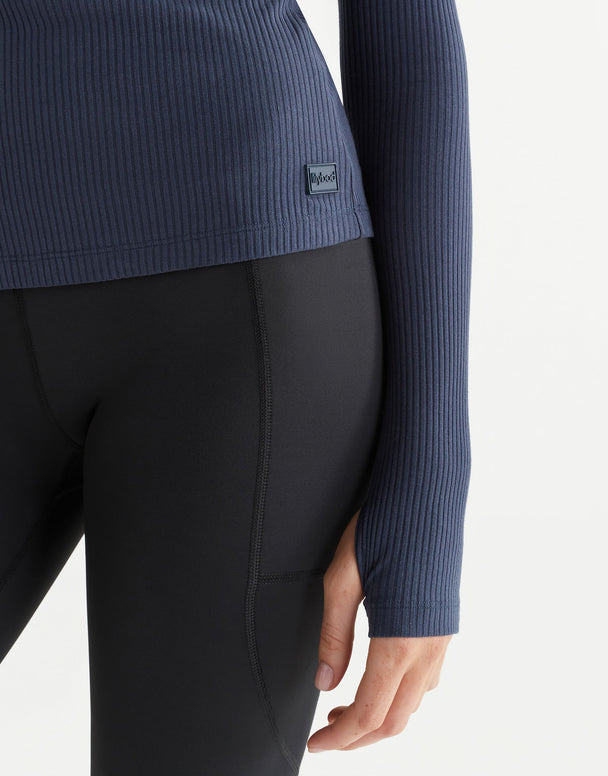 Person wearing a blue ribbed sweater and black leggings on a white background