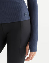 Person wearing a blue ribbed sweater and black leggings on a white background