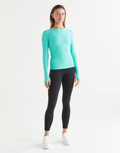 Woman wearing a turquoise long-sleeve top and black leggings on a white background