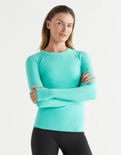Woman wearing a turquoise long-sleeve top against a white background