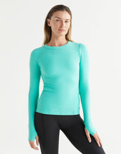 Woman wearing a teal long-sleeve athletic top and black leggings on a white background